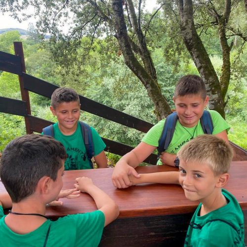 Cuatro niños sentrados sobre una mesa en el bosque durante una actividad del campamento de verano multiaventura